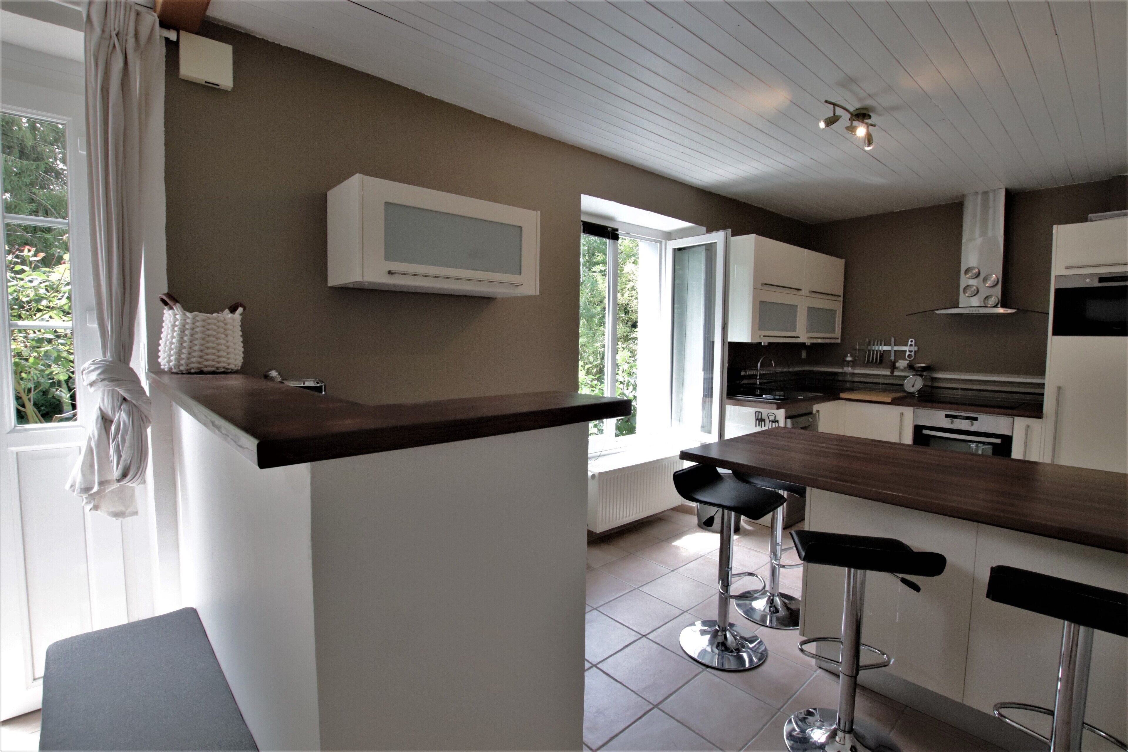 Una cocina moderna con armarios blancos, encimera de madera y dos taburetes negros.