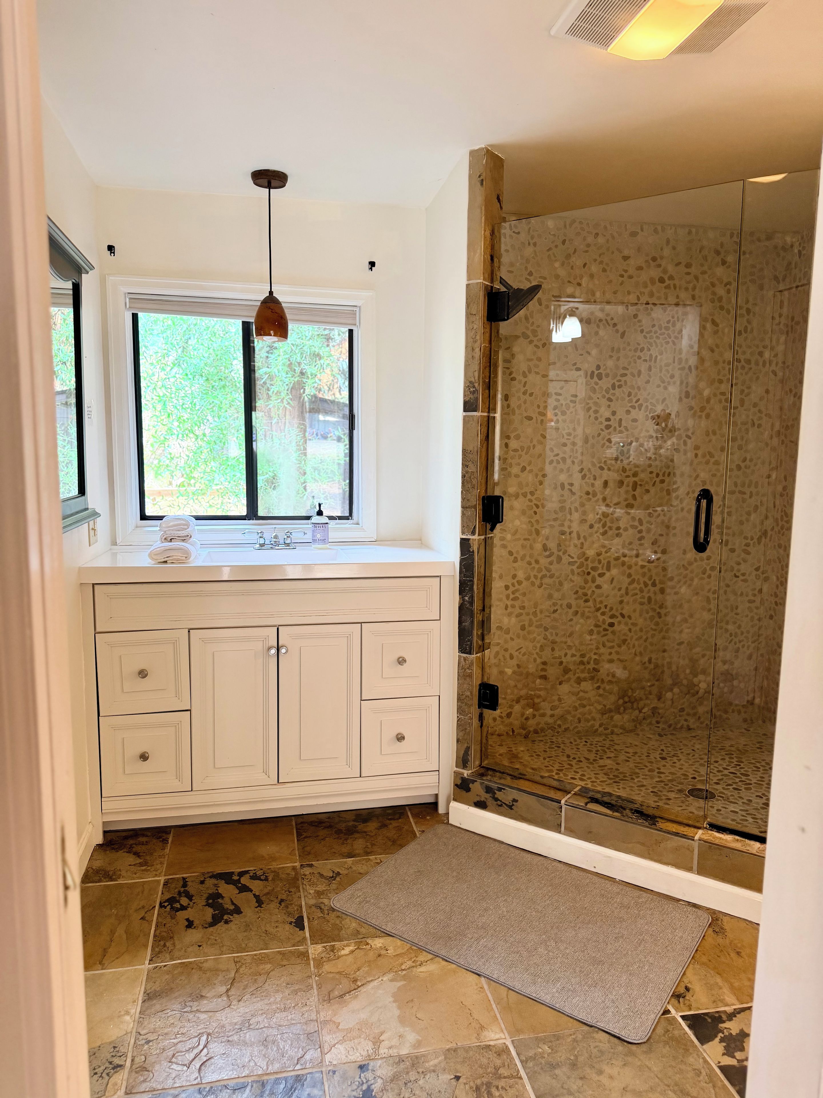 A bathroom with a shower, a window, and a sink.