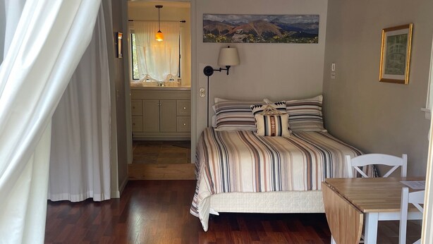A bedroom with a wooden floor, a bed with striped bedding, a bedside table, a chair, and a painting on the wall. - The Guest Cottage in Lake City (Lake City)