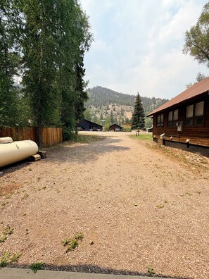 Un chemin de gravier mène à un chalet en bois, avec une vue sur les montagnes en arrière-plan.
