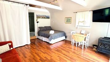 A spacious room with a wooden floor, a bed, a red sofa, a dining table with chairs, and a television.