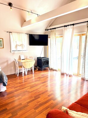 Un salon avec un plancher en bois, un téléviseur fixé au mur, une table à manger avec des chaises et un canapé rouge.