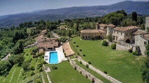 A large estate with a swimming pool, stone buildings, and expansive green lawns.
