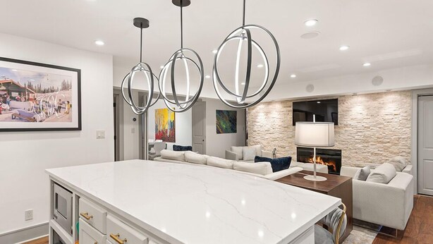 A modern kitchen with a large island, pendant lighting, a stone accent wall, a fireplace, and a living area with a sofa and a painting. - BRIGHT, Renovated, In the Heart of Aspen Walkable (Aspen)
