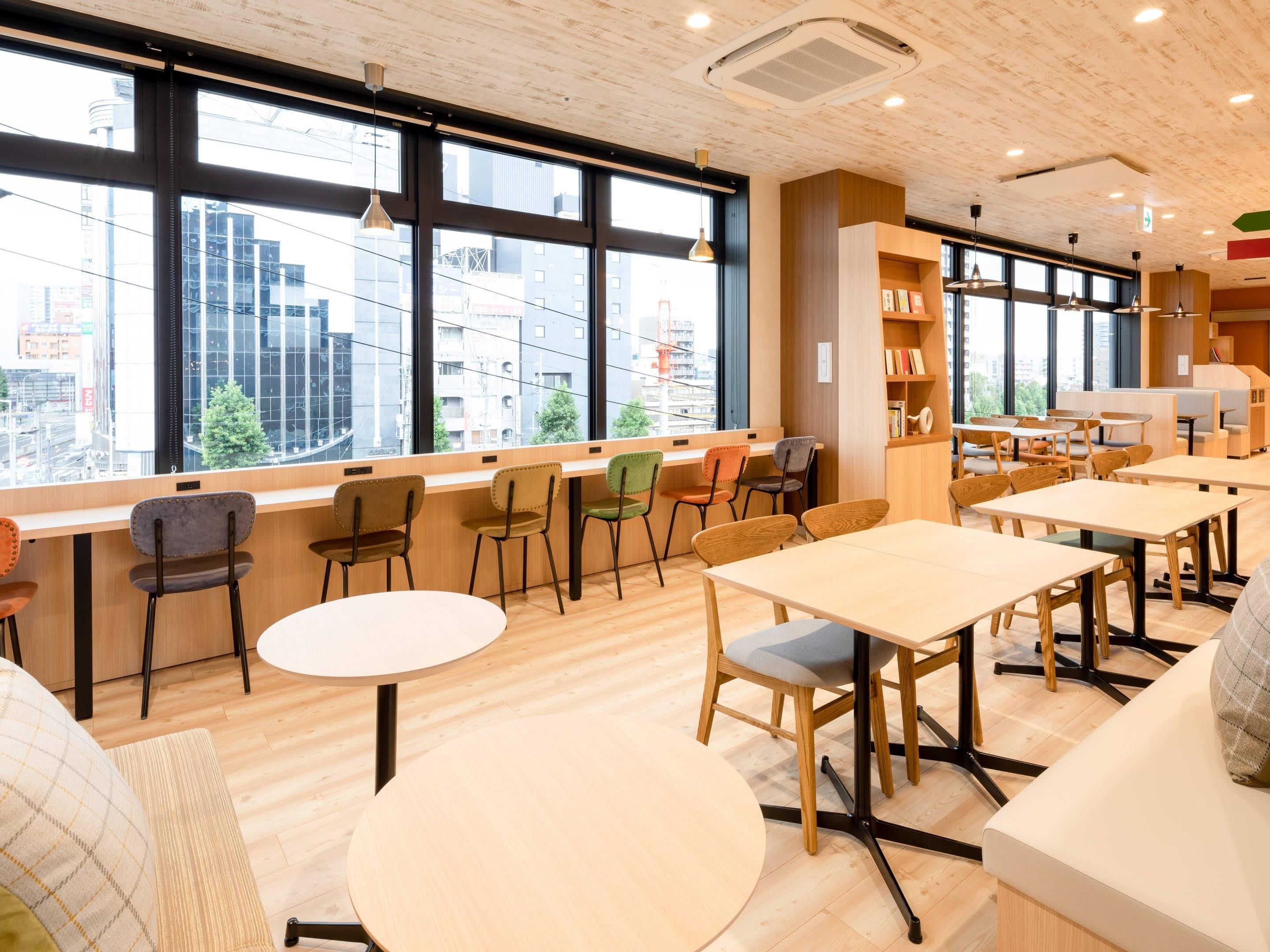 Un interior moderno con amplios ventanales, suelo de madera y diversas opciones de asiento, incluidas mesas y sillas.