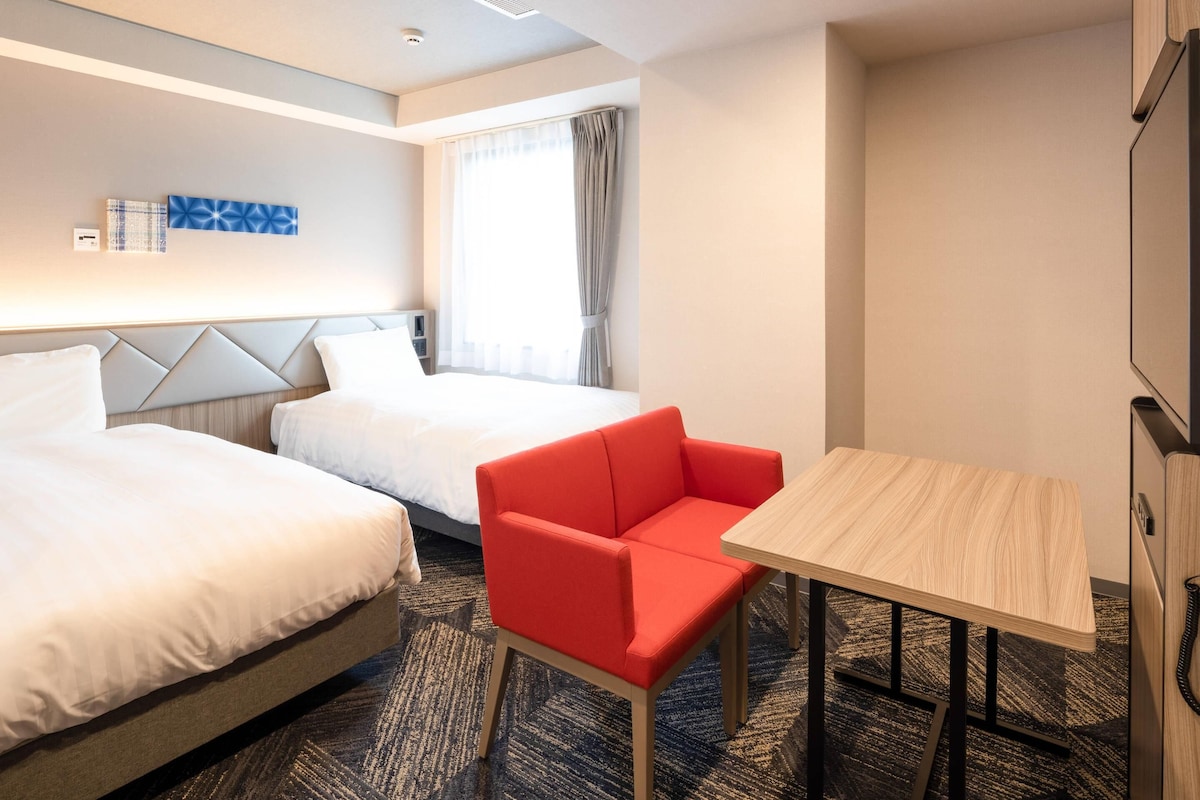 A hotel room with two beds, a red chair, a small table, and a TV.