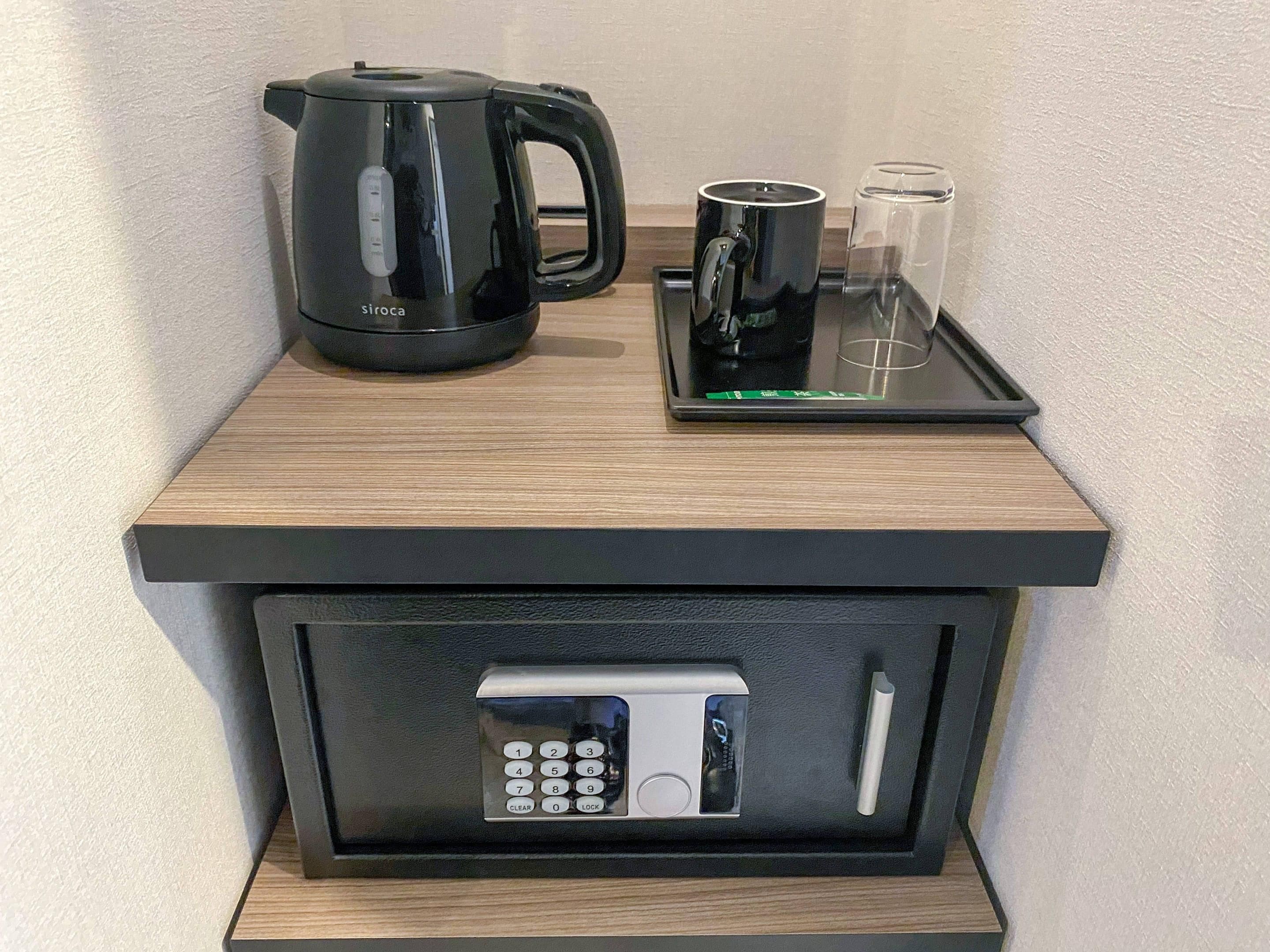 Un minibar con una cafetera, vasos y un control remoto.