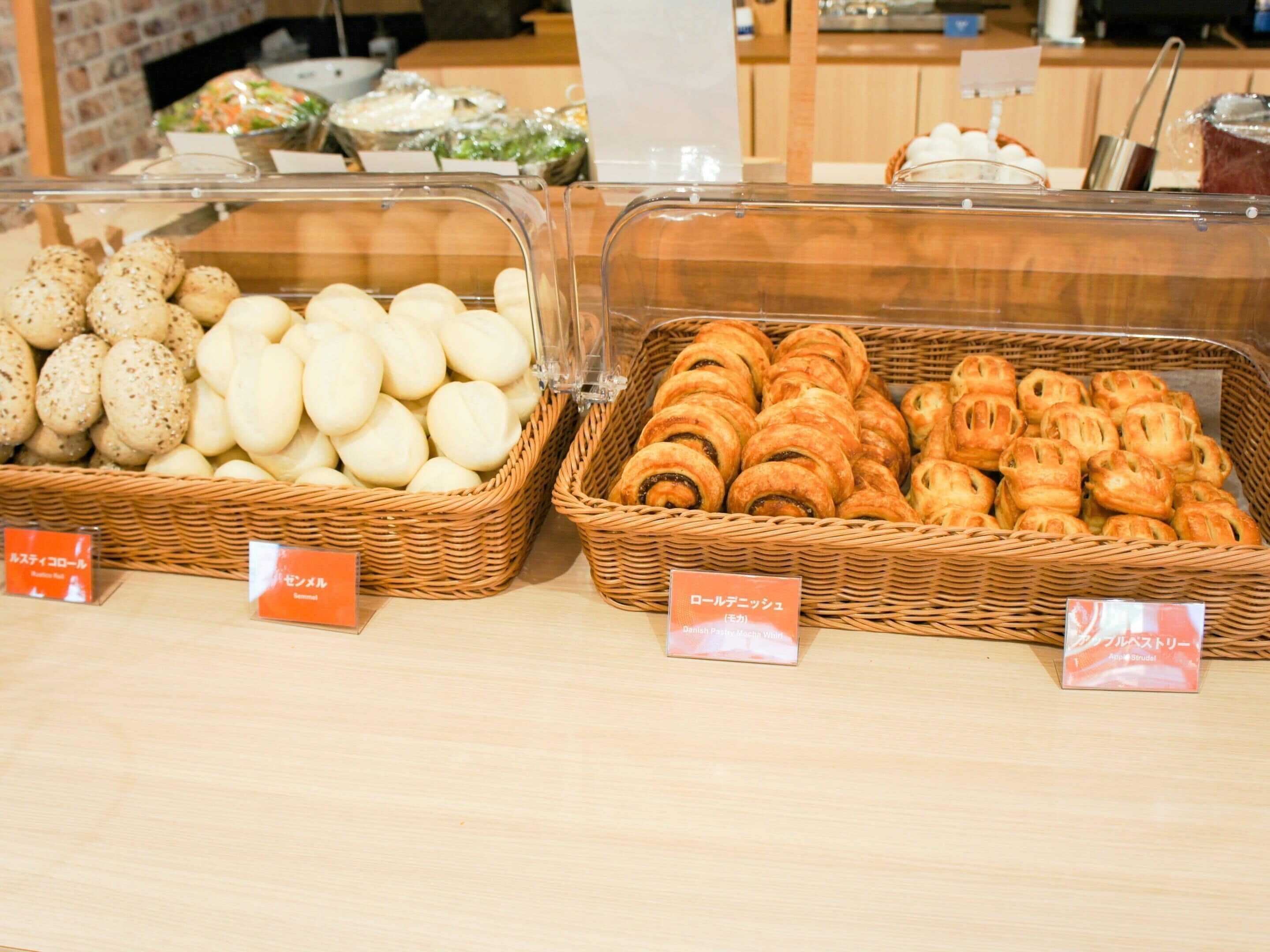 Una vitrina de panadería con diversos productos horneados en cestas de mimbre, con sus nombres identificados.