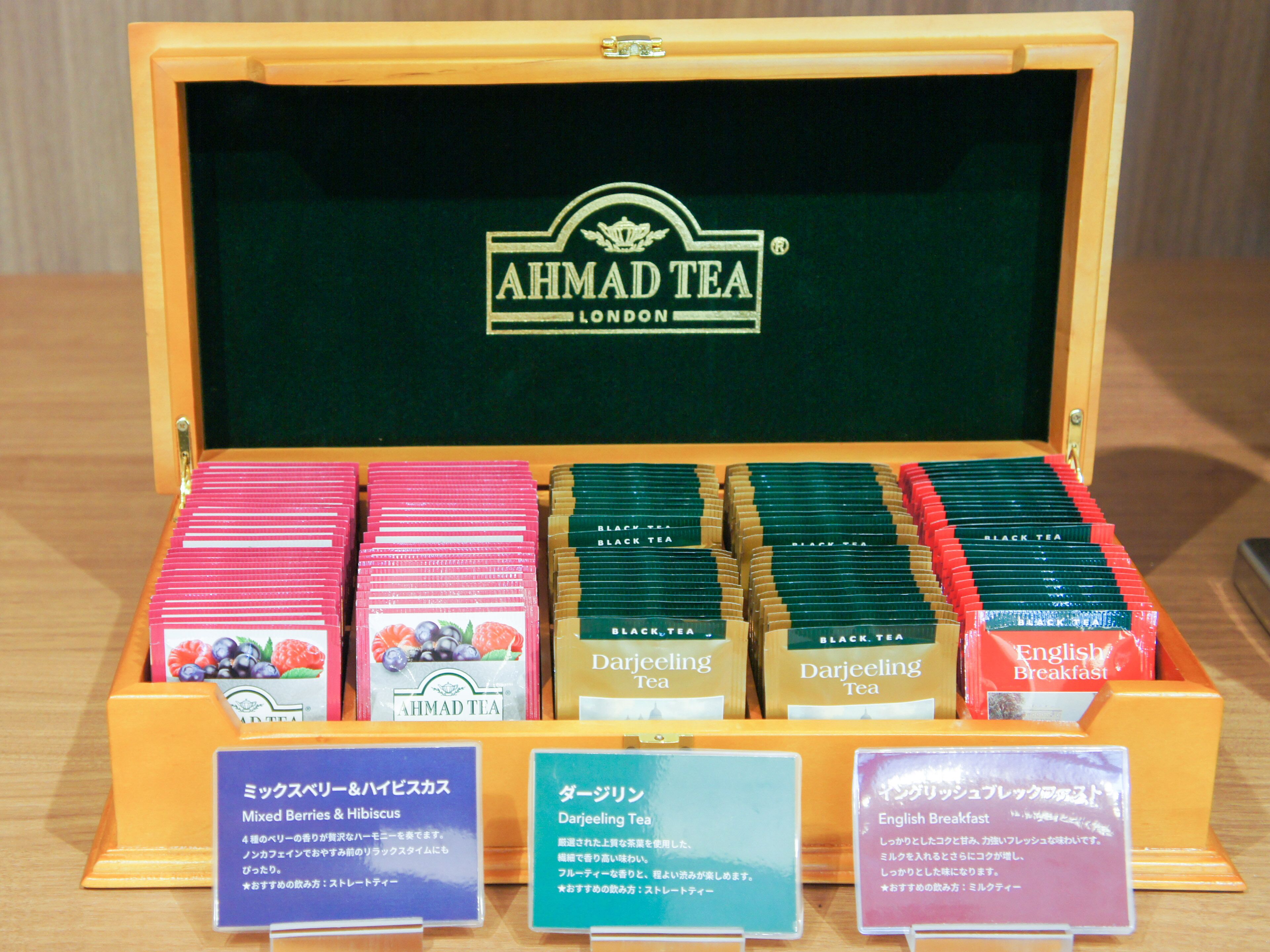 Une sélection de produits AHMAD TEA présentée dans une boîte en bois, avec des étiquettes en anglais et en japonais.