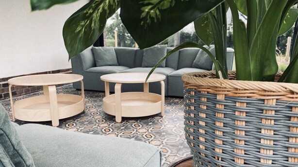A cozy seating area with a grey sofa, two round wooden tables, and a large woven basket.