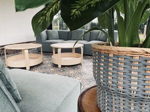 Una zona de estar acogedora con un sofá gris, dos mesas redondas de madera y una cesta grande de fibras.