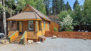 A small wooden cabin with a porch, a fenced yard, and a gravel driveway. - Pet-Friendly Chic Downtown Home w/ Queen Suite & Desk | Near River & Bike Trails (Truckee)