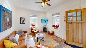 A living room with a brown leather sofa, a coffee table, a wooden door, and a ceiling fan. - Pet-Friendly Chic Downtown Home w/ Queen Suite & Desk | Near River & Bike Trails (Truckee)