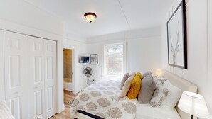 A bedroom with a bed, a bedside lamp, a wall-mounted fan, a window, and a door. - Pet-Friendly Chic Downtown Home w/ Queen Suite & Desk | Near River & Bike Trails (Truckee)