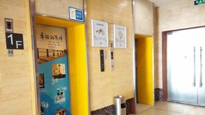 A hallway with a blue door labeled '1F', a trash bin, and a wall with two framed certificates. - 7 Days Inn (Qiannan)