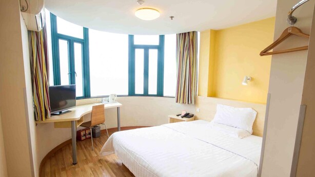Una habitación de hotel con una cama, un escritorio con computadora, una silla y una ventana con cortinas.