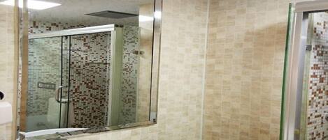 Un baño con un lavamanos blanco, cabina de ducha con mampara de vidrio y pared con azulejos.