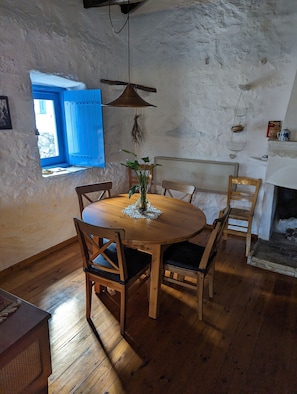 Uma área de jantar rústica com uma mesa redonda de madeira, quatro cadeiras e um lustre.