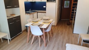 A compact kitchen with a microwave, stove, and dishwasher. A dining table with chairs is set for four. - Appartement en Centre Ville Avec Terrasse Exposée Ouest (Cauterets)