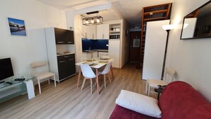 A compact living space with a dining area, kitchenette, and a TV on a glass table. - Appartement en Centre Ville Avec Terrasse Exposée Ouest (Cauterets)