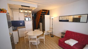 A compact living space with a kitchenette, a dining area, and a red sofa. - Appartement en Centre Ville Avec Terrasse Exposée Ouest (Cauterets)