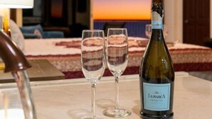 Une chambre avec un lit, une bouteille de vin et deux verres sur une table.
