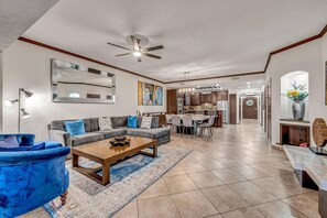 A spacious living room with a sofa, coffee table, and a dining area with chairs and a kitchen in the background.