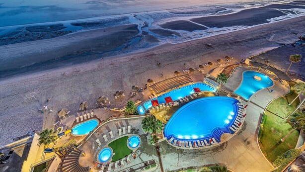 Vue aérienne d’un complexe hôtelier doté de plusieurs piscines, d’une plage et d’un coucher de soleil.