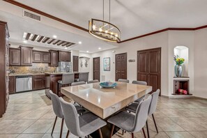 A modern kitchen with dark wood cabinets, a large island, and a dining area with a rectangular table and six chairs.