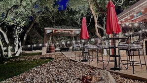 Un área de estar al aire libre con mesas y sillas, sombrillas rojas y una estructura de pérgola.