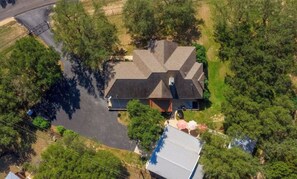 Vue aérienne d’une maison à toit en pente, entourée d’arbres denses.