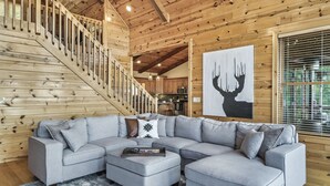A modern living room with a grey sectional sofa, a wooden staircase, and a kitchen in the background. - Game Rooms + Views: Spacious Mtn Cabin in Murphy! (Murphy)