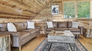 A cozy cabin interior with wooden walls, two leather sofas, a coffee table, and a window with blinds. - Game Rooms + Views: Spacious Mtn Cabin in Murphy! (Murphy)