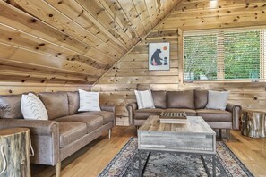A cozy cabin interior with wooden walls, two brown leather sofas, a wooden coffee table, and a large window with blinds. - Game Rooms + Views: Spacious Mtn Cabin in Murphy! (Murphy)