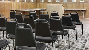 A conference room with rows of black chairs, a wooden panel wall, and a tiled floor. - Courtyard Hotel & Event Center (Crockett)