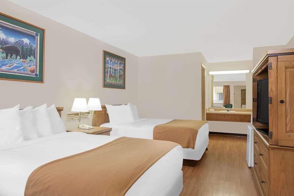 A hotel room with two beds, a television, a mirror, and artwork on the walls.