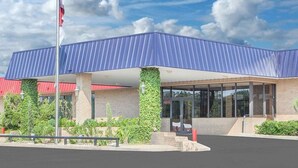 A modern building with a blue roof, brick walls, and a covered entrance area with glass doors. - Courtyard Hotel & Event Center (Crockett)