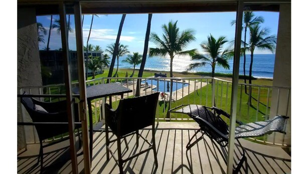 Un balcon avec vue sur l’océan, les palmiers et une piscine.