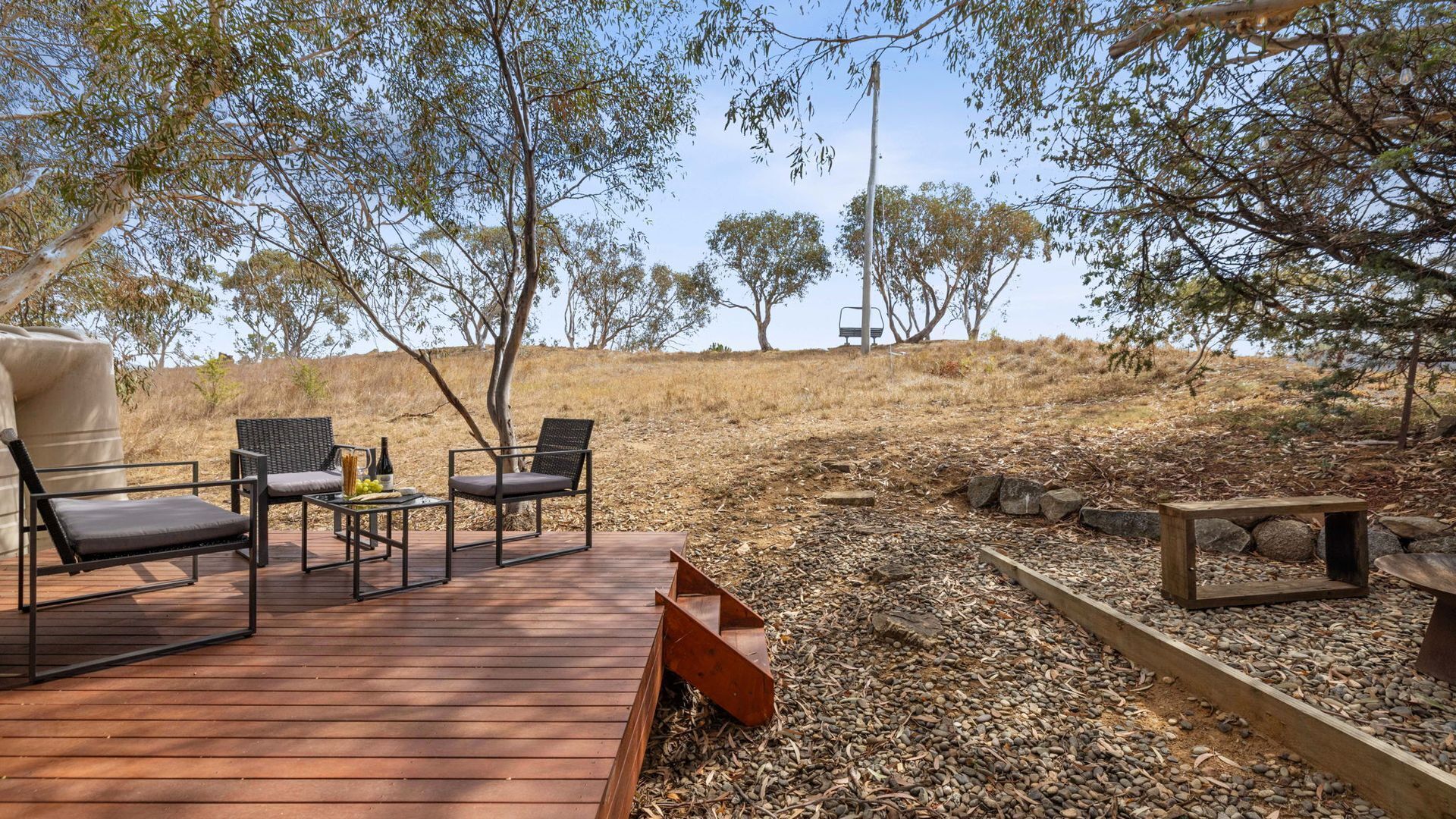 Une terrasse dotée de mobilier d’extérieur, une table avec une bouteille et des raisins, et une vue sur les arbres et les collines.