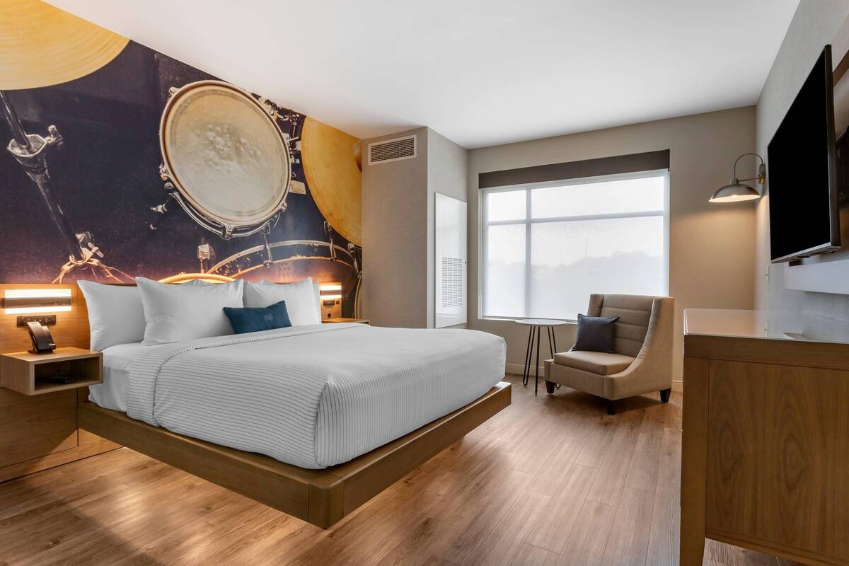 A modern hotel room with a bed, a chair, a desk, and a large window.