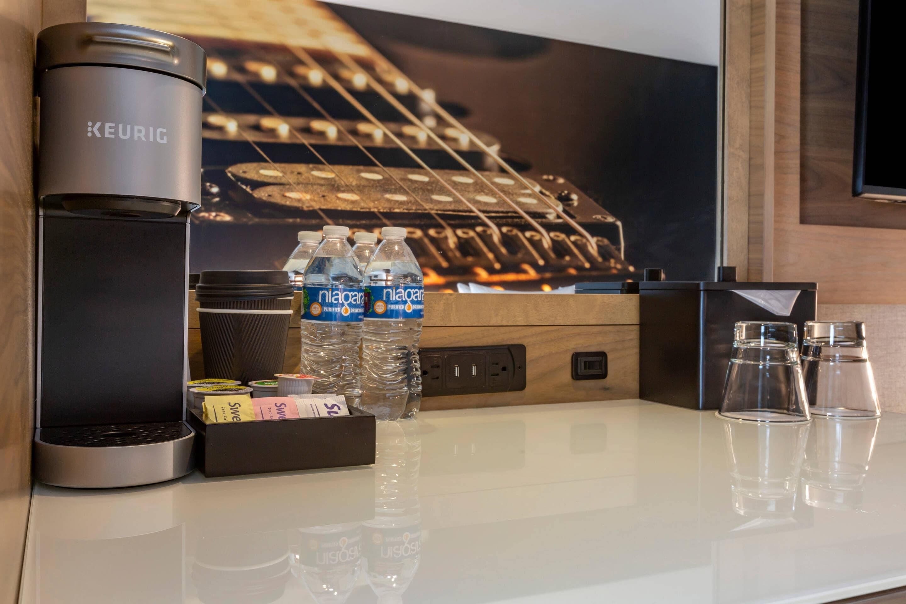 A minibar with a Keurig coffee maker, water bottles, and a box of tissues.