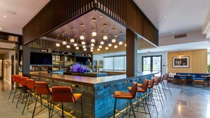 Zona de bar moderna con mostrador, taburetes y luminarias colgantes.