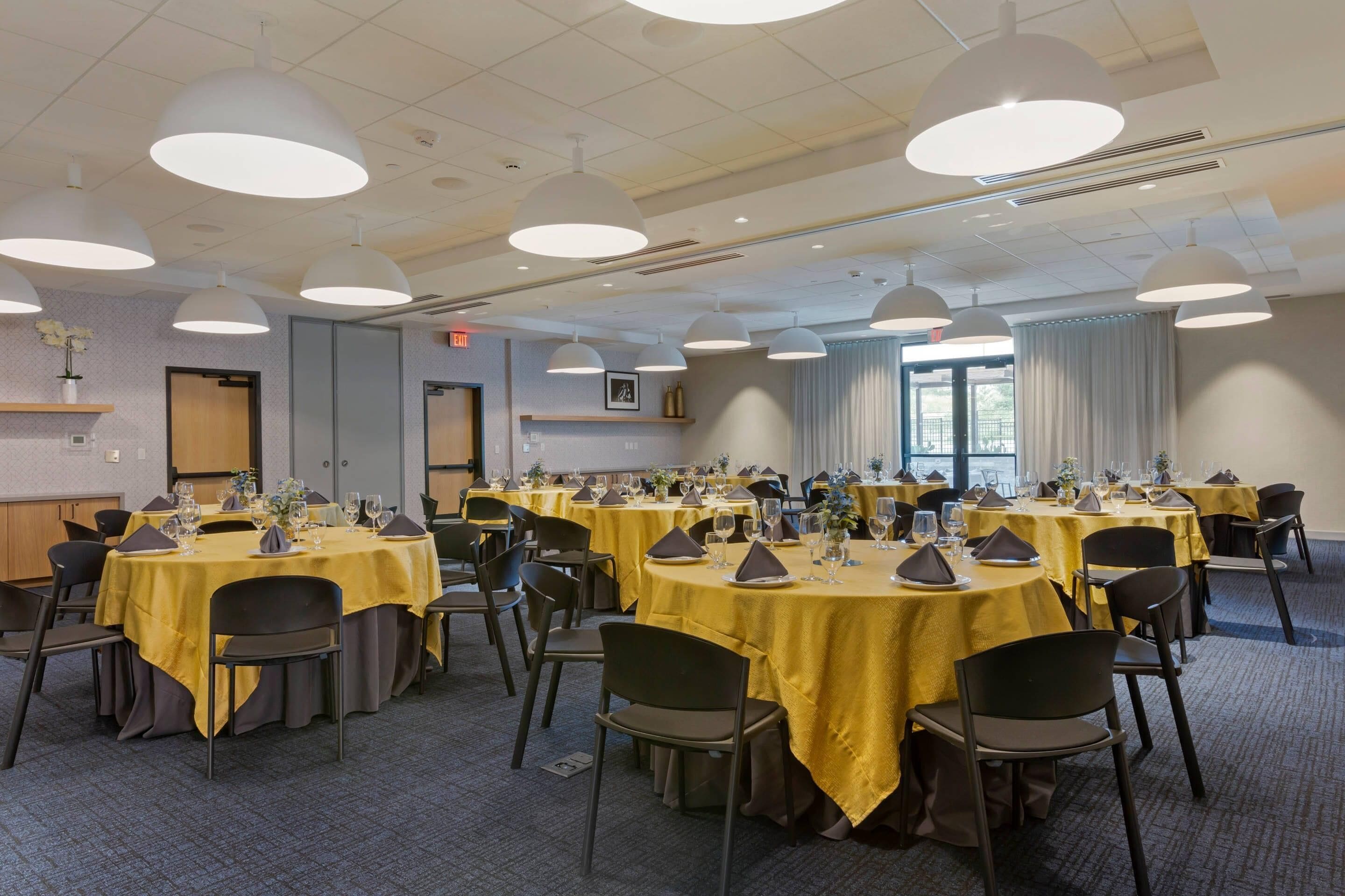 A conference room with multiple tables, chairs, and pendant lighting.