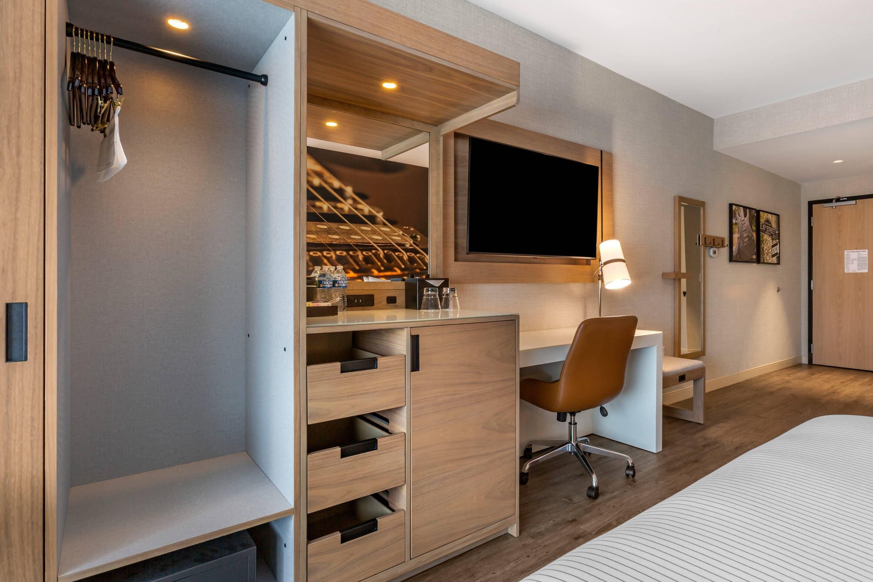 A hotel room with a bed, a desk, a chair, a TV, a wardrobe, and a mirror.