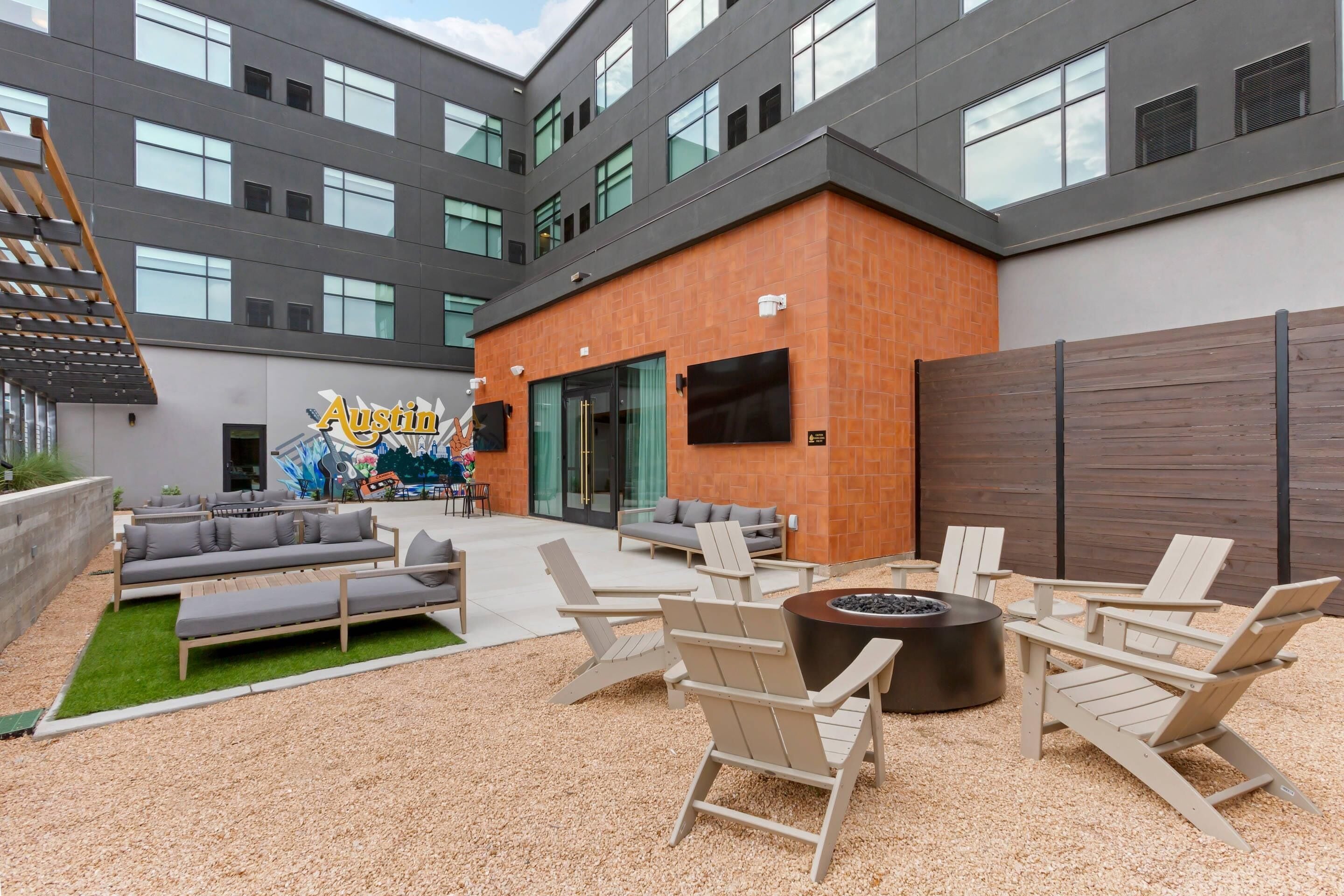 Un patio con mobiliario exterior, una fogata y un edificio con un mural.
