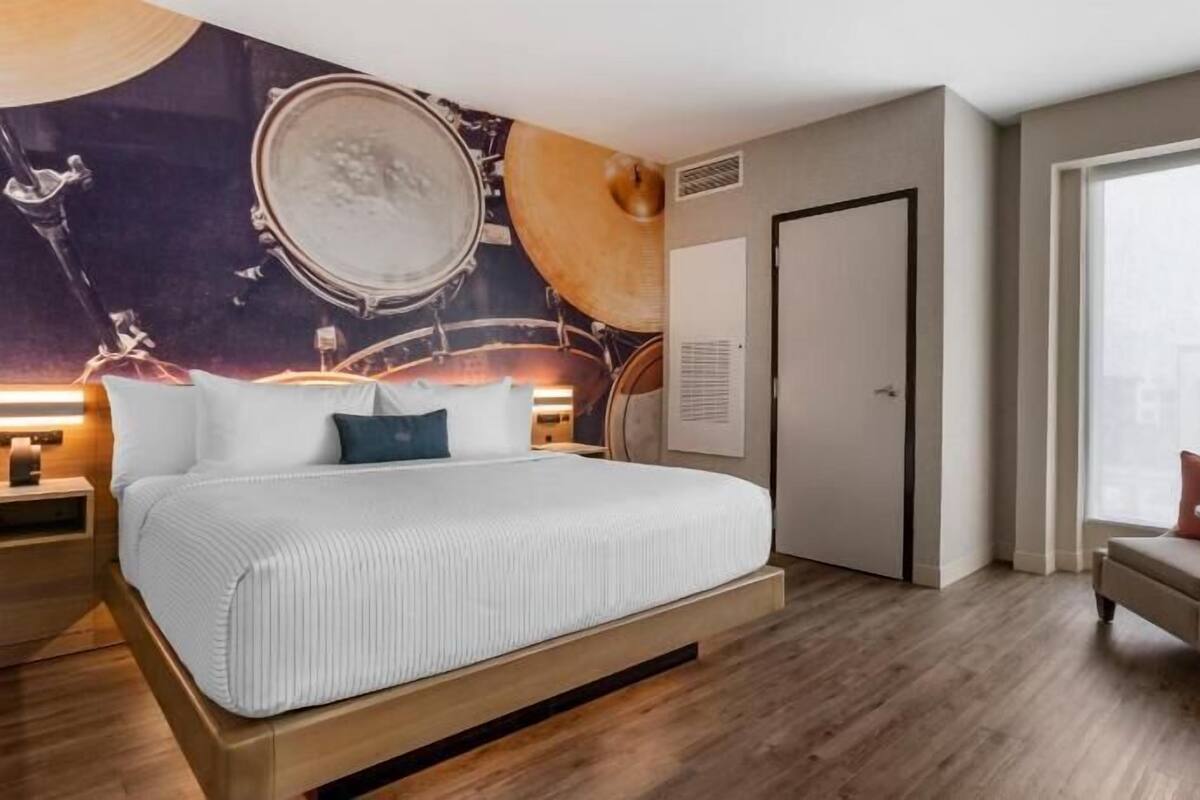 A modern hotel room with a large bed, a small round table, a sofa, and a large window.