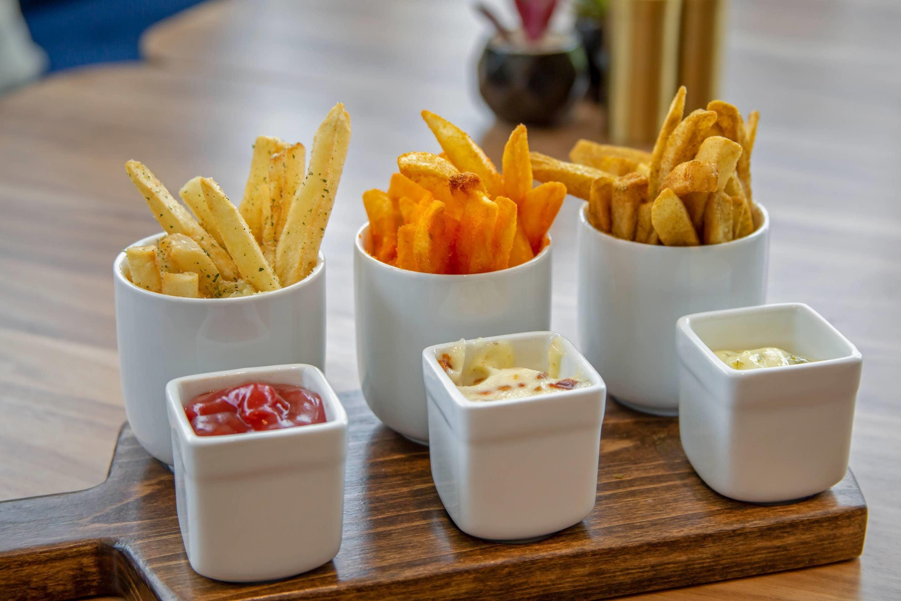 A tray with three small bowls of fries and two small bowls of condiments.