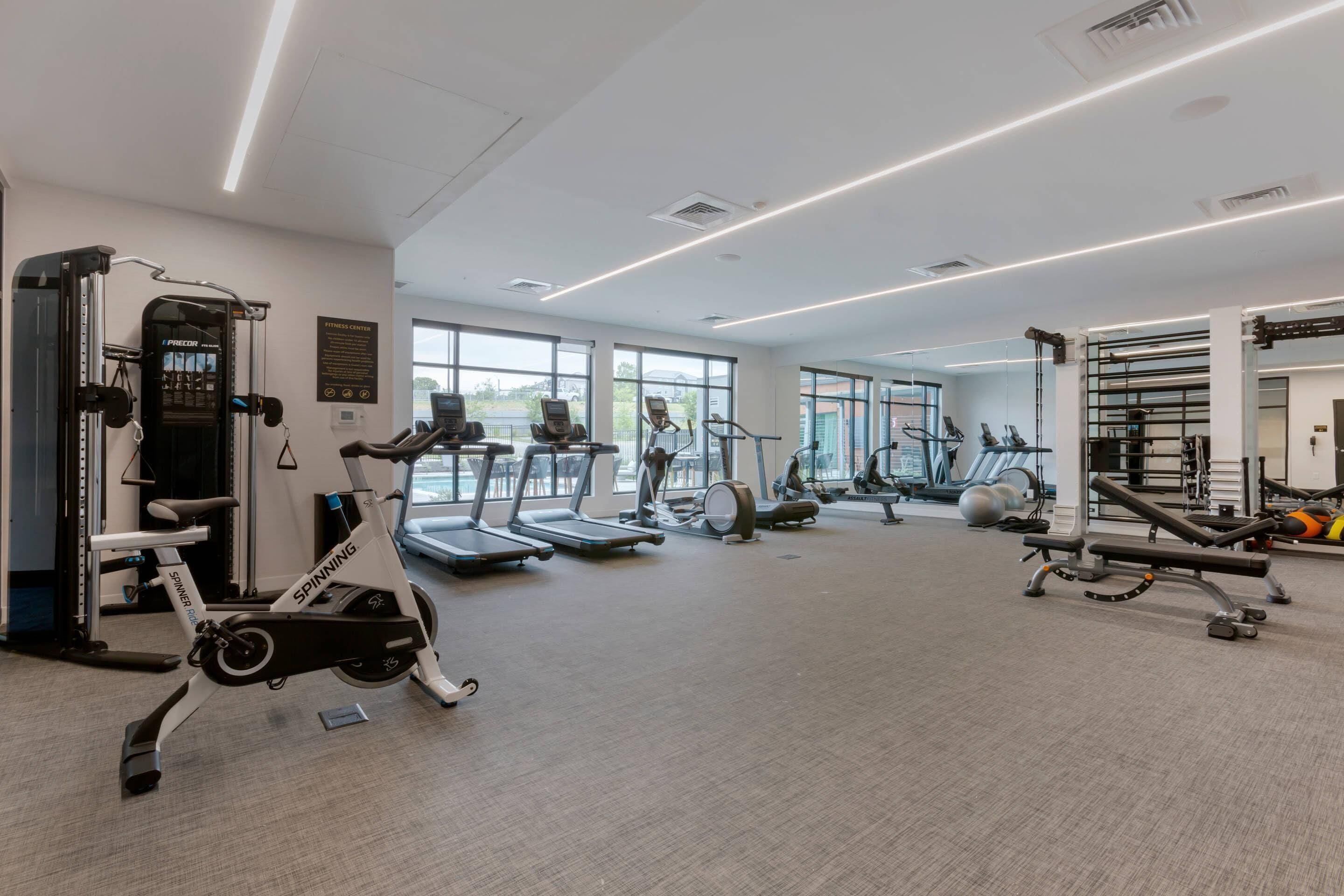 Un gimnasio con máquinas de cardio, equipo de pesas y amplias ventanas.