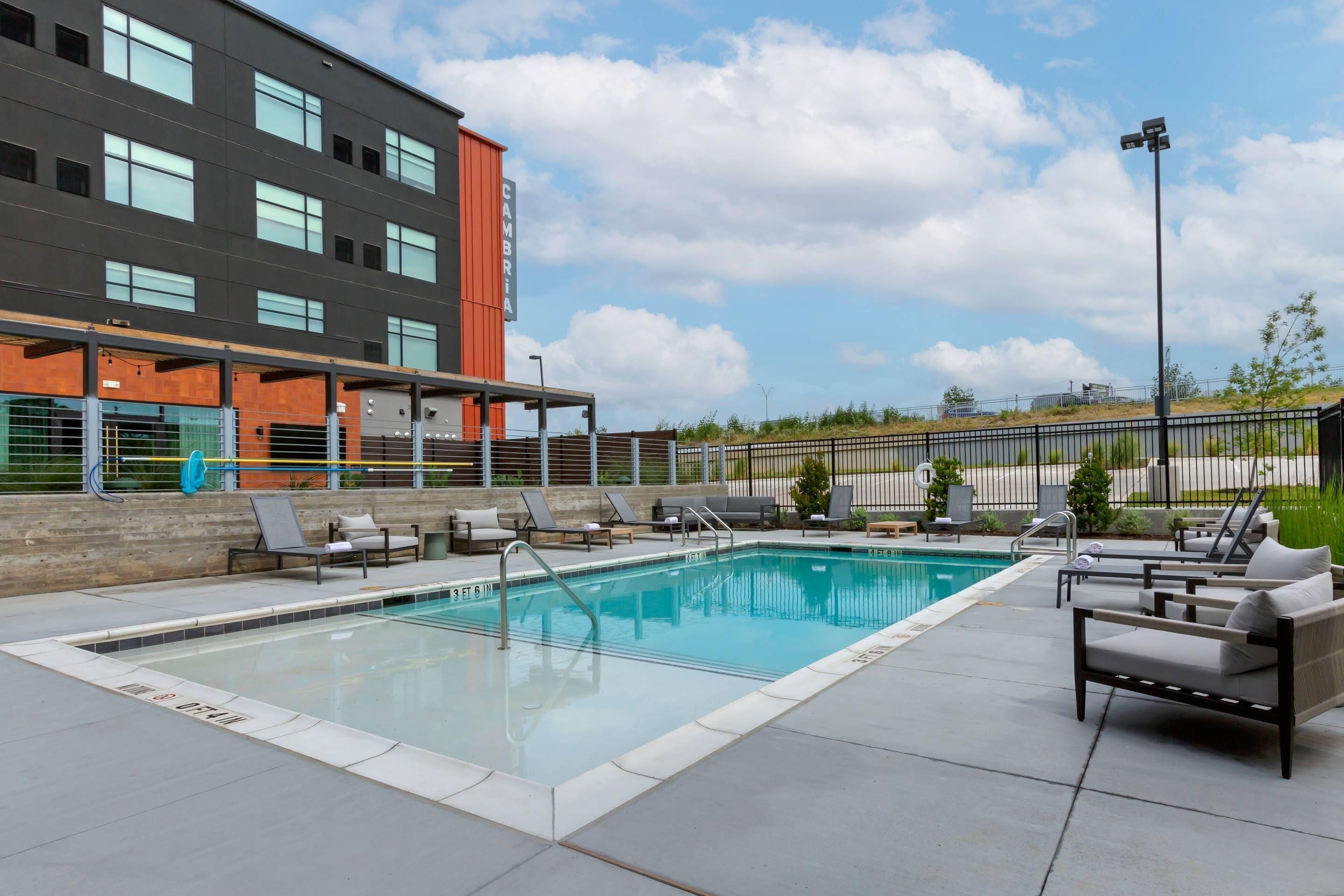 A swimming pool with lounge chairs, a building with multiple windows, and a clear sky.