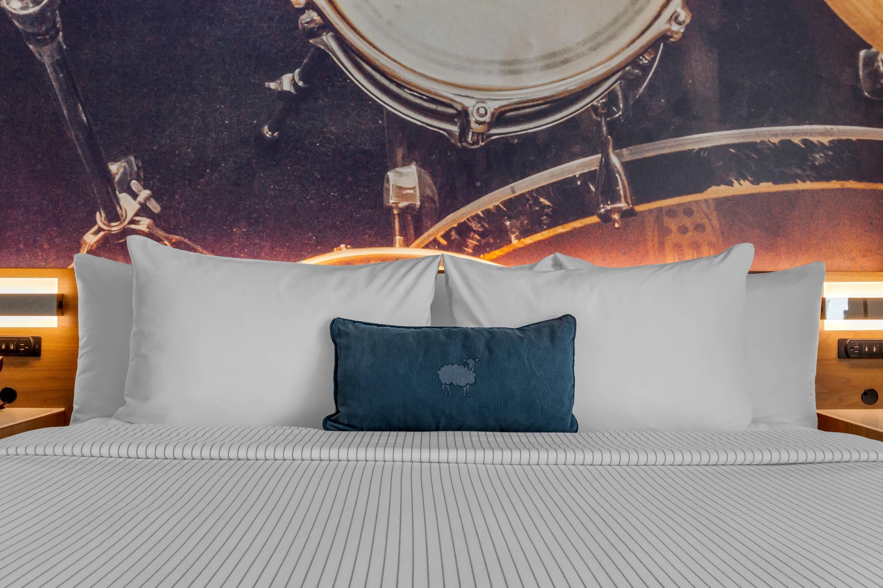 Un lit avec une literie à rayures, un oreiller bleu orné d’un motif de mouton et une fresque murale représentant une scène spatiale.